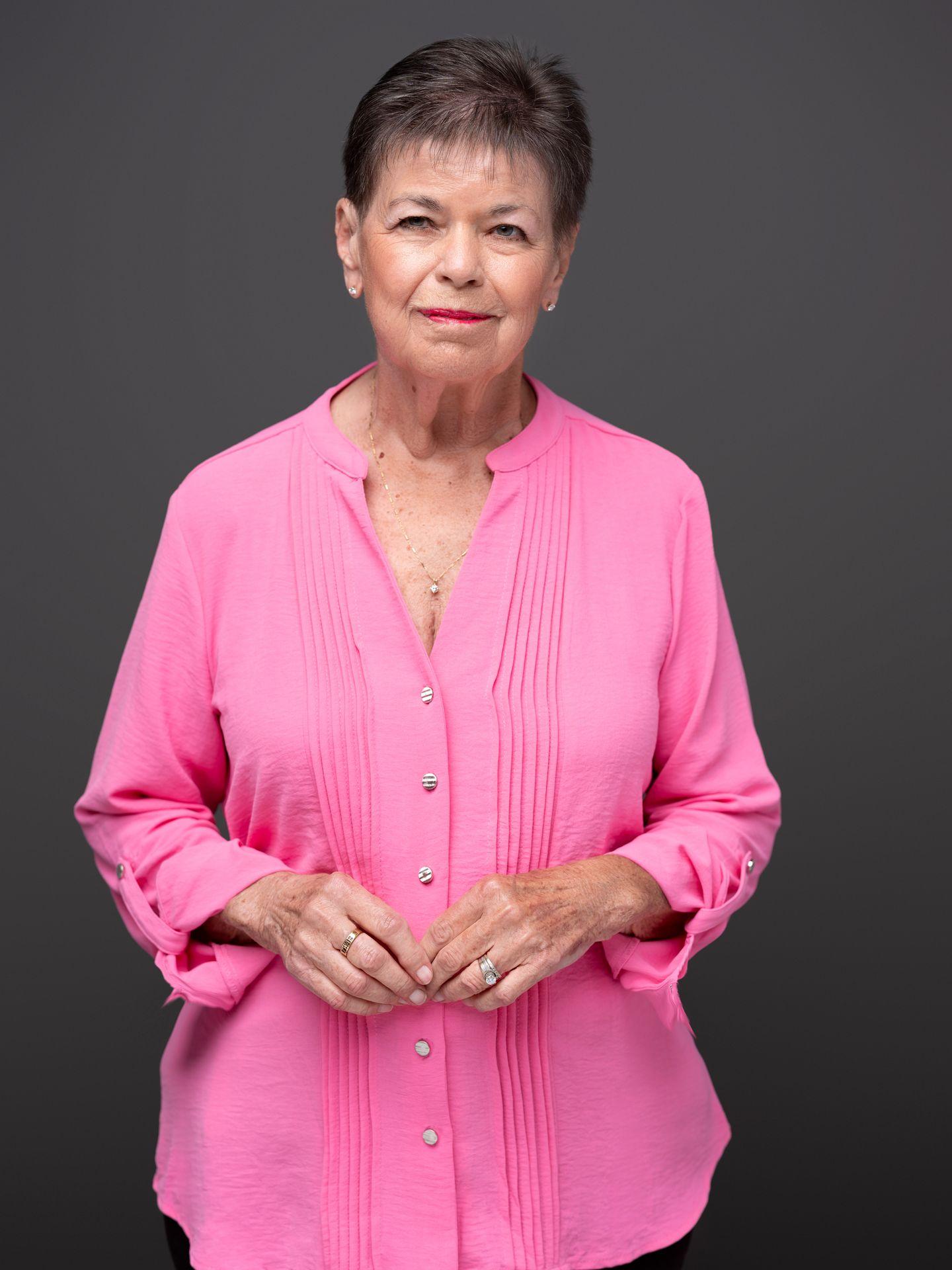 Person wearing a bright pink blouse with their hands clasped together.